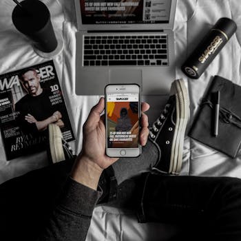 Overhead view of a stylish workspace with laptop, smartphone, magazine, and personal items.